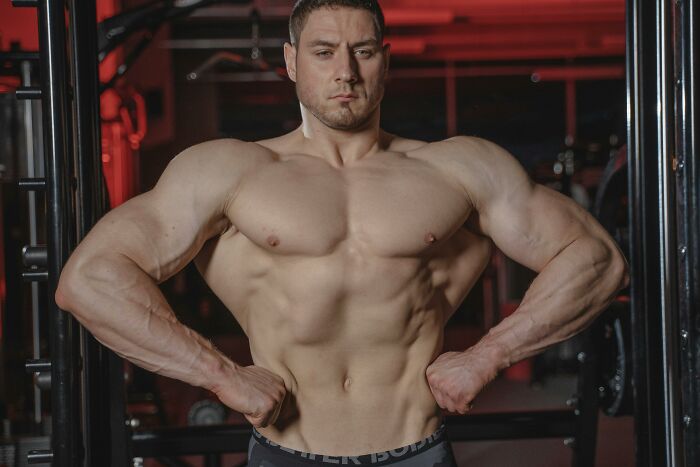 Muscular man posing in a gym, showcasing strength and fitness amidst intense workout equipment.