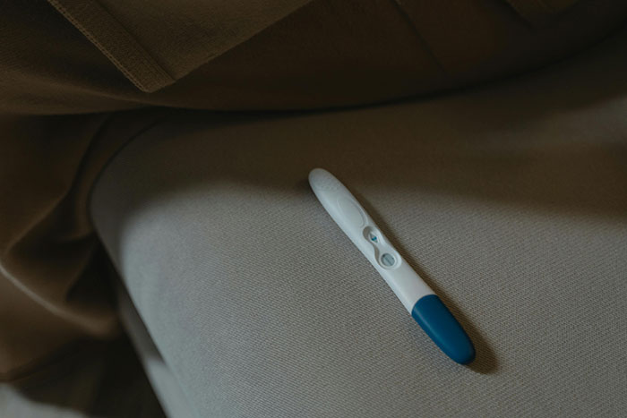 Positive pregnancy test resting on a gray fabric surface, symbolizing manipulative mom daughter story drama themes. - 25