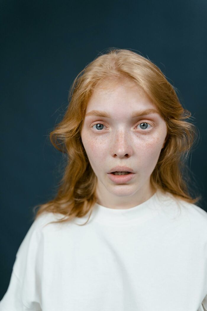 Young woman with red hair and freckles looks shocked and disturbed against a dark background, reflecting disturbing things overheard.