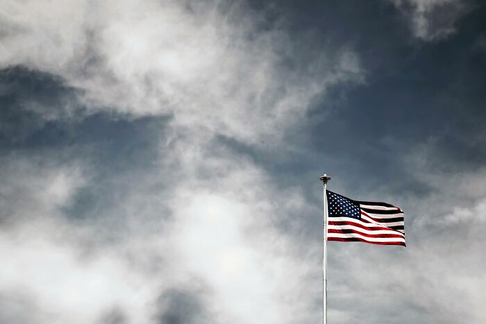 American flag waving against a cloudy sky, illustrating themes of harmless lies parents told that left kids low key traumatized - 22