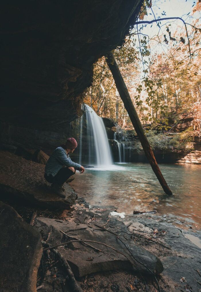 Person sitting near a waterfall in a forest, exploring nature and contemplating survival tips in a peaceful outdoor setting.