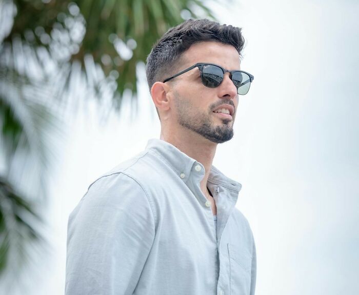 Man wearing sunglasses and a light shirt outdoors with palm leaves, representing what makes a man instantly unattractive.