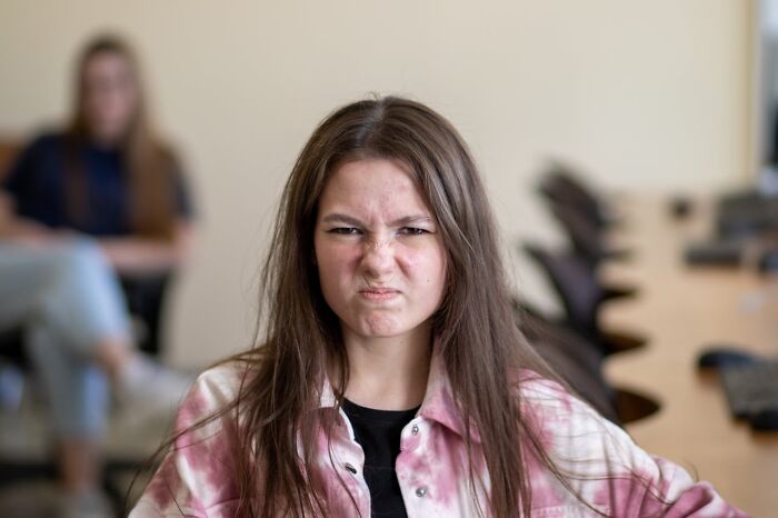 Young woman in a pink shirt making an angry face, representing entitled patients demanding special treatment.