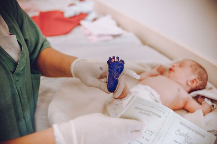 Medical professional in gloves holding a newborn’s inked foot for identification in a hospital setting. - 4