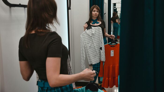 Woman holding clothes and looking in the mirror, illustrating pettiest things in breakups and borderline insane emotions.