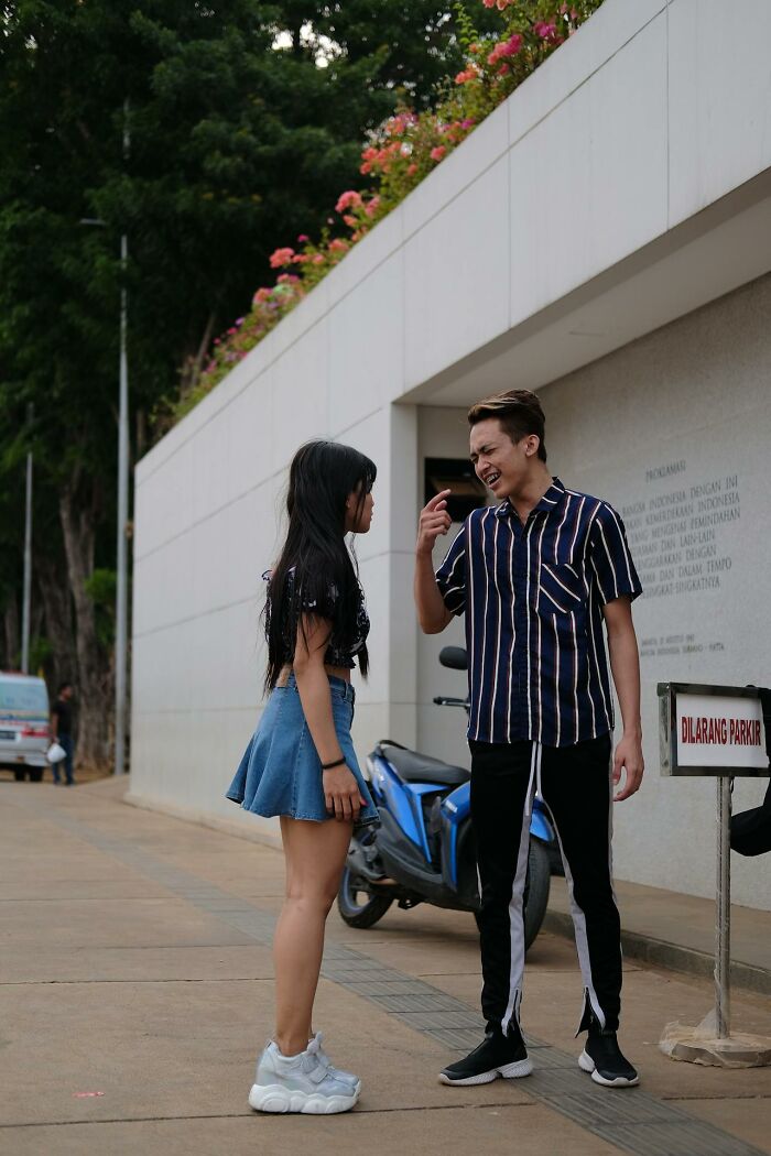 Young man and woman having a disturbing conversation outdoors near a parked motorbike and a no parking sign.