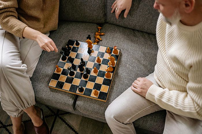 Two people playing chess on a couch, illustrating tension between a person and their grifter neighbor over money issues.