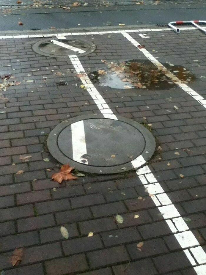 Parking lines painted over two manhole covers on brick pavement, illustrating engineering mistakes.
