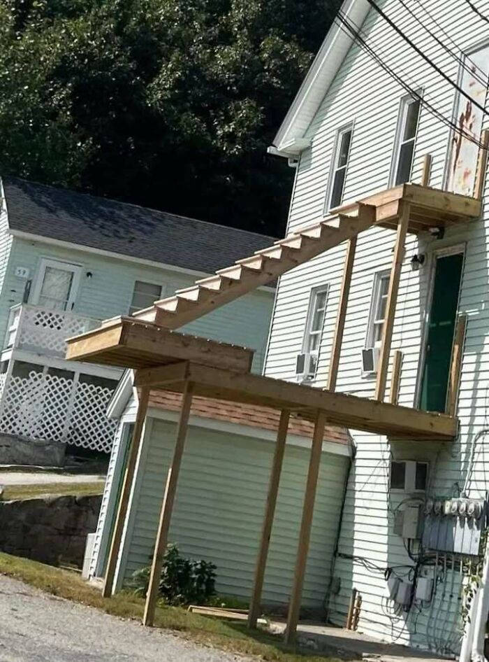 Poorly designed engineering mistake showing broken stairs leaning on an unfinished porch structure outside a house.
