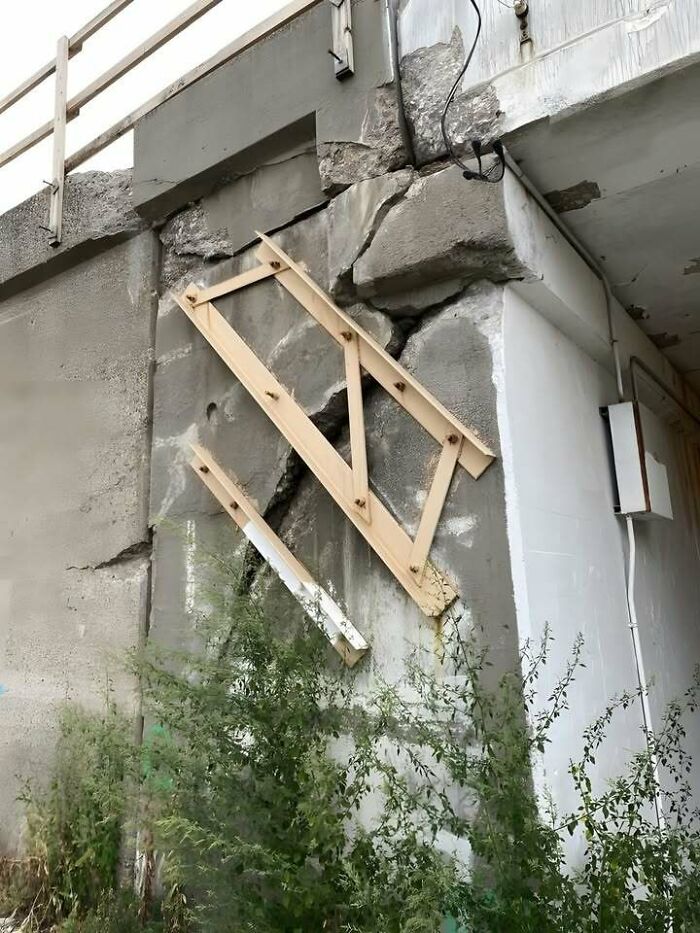 Wooden braces fixed at odd angles on a c*****d concrete wall showing engineering mistakes outdoors.