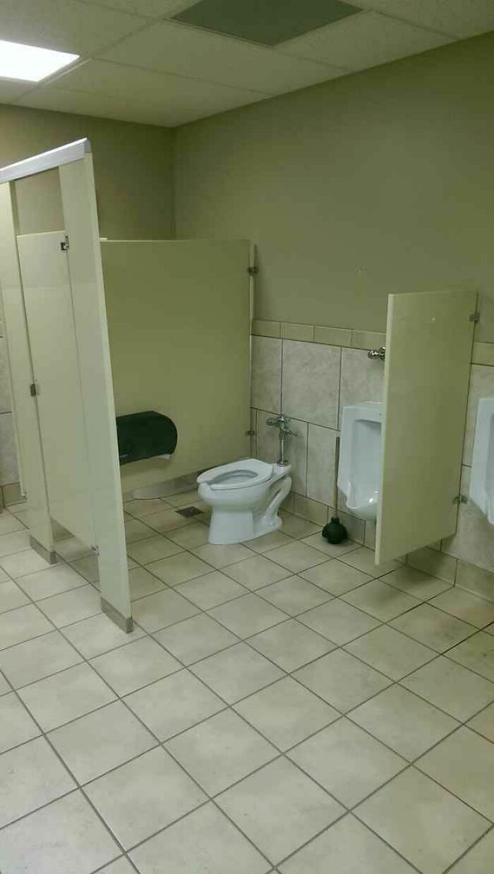 Public restroom with a toilet placed outside the stall, showcasing hilariously dumb engineering mistakes.