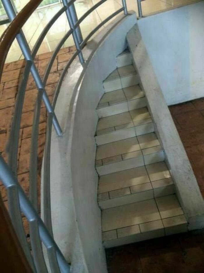 Narrow curved staircase with poorly designed steps and railing causing a hazard in engineering construction.