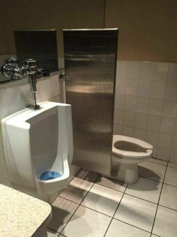 Restroom with a urinal and toilet separated by a short, ineffective privacy divider in an engineering design fail.