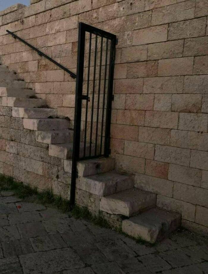 Stone staircase blocked by a metal gate, an example of hilariously dumb engineering mistakes in construction.