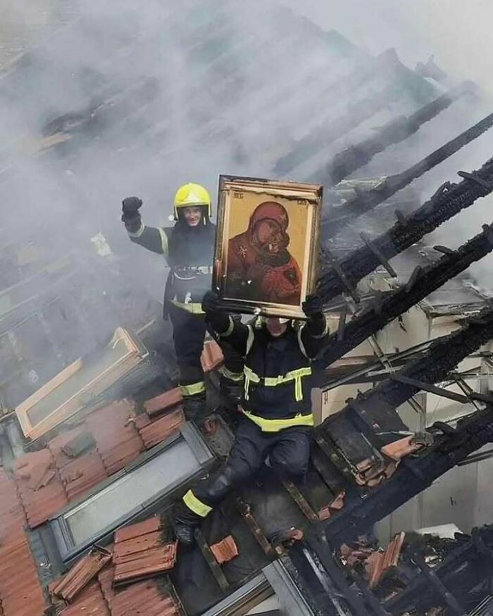 Firefighters rescue a religious icon from a burnt building, combining trash and culture in chaotic ways.