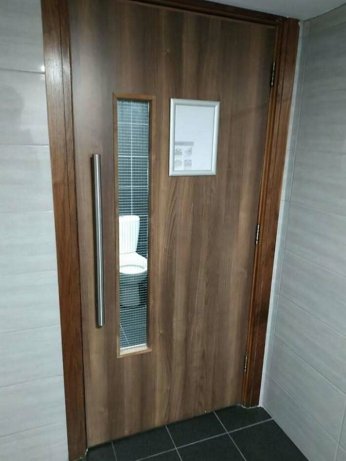 Wooden door with a vertical window showing a toilet inside, highlighting hilariously dumb engineering mistakes.