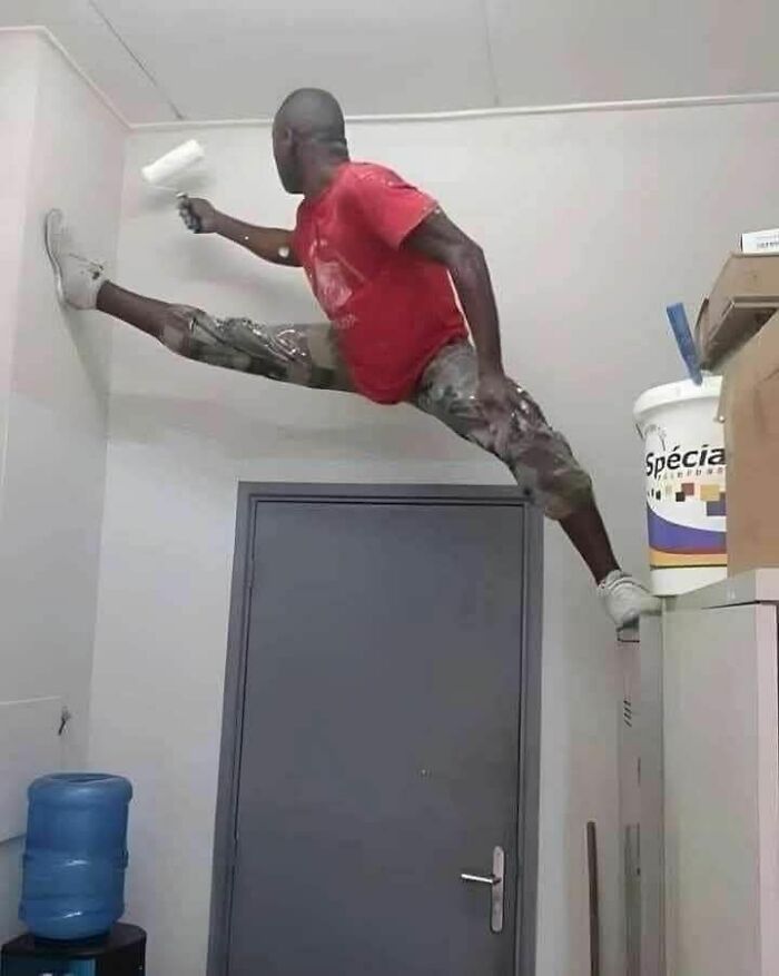 Man doing an extreme split between wall and cabinet while painting a wall, showing hilariously dumb engineering mistakes.