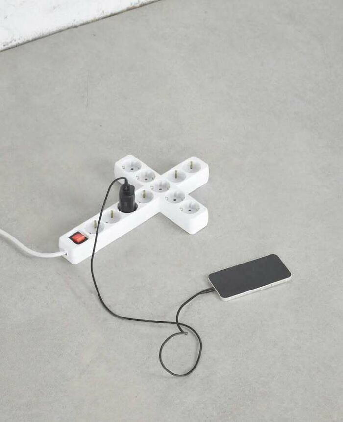 Power strip shaped like a cross with a phone charging, combining trash and culture in a chaotic way.