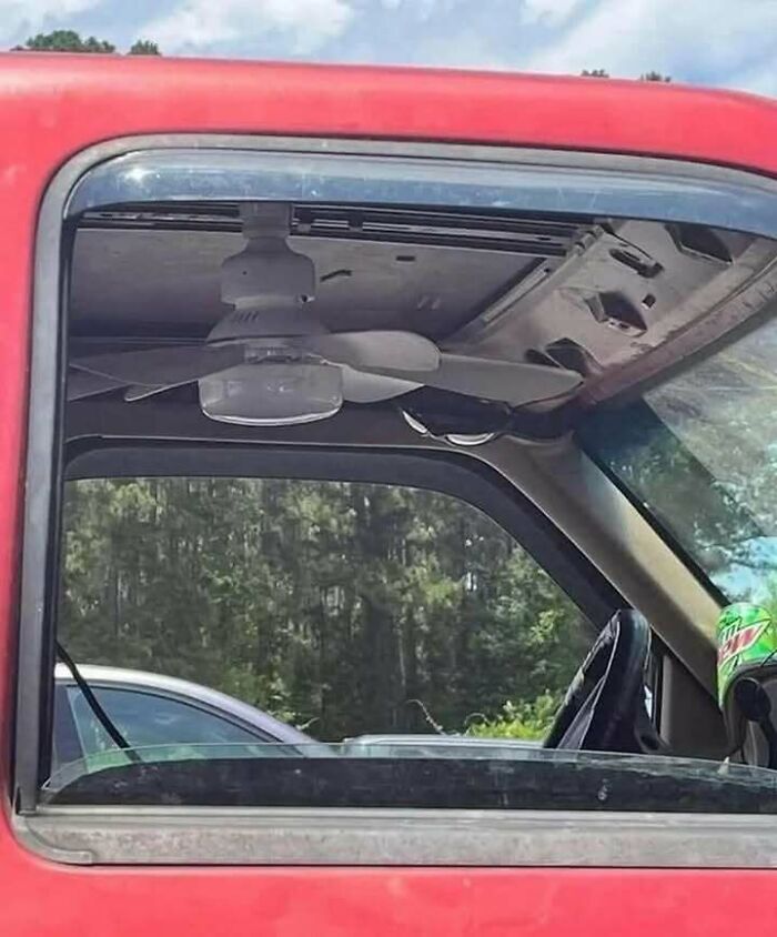 Old red truck with a ceiling fan installed inside the cab, showcasing chaotic and funny trash culture creativity.