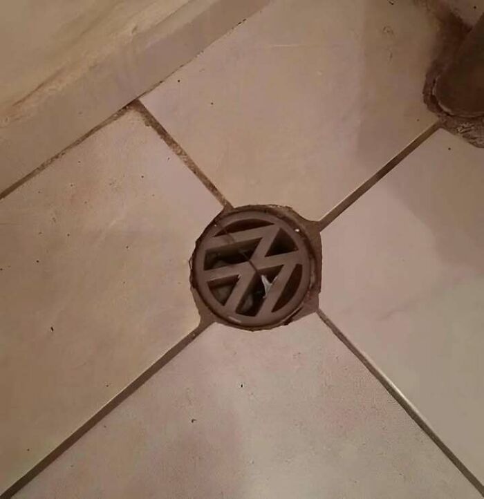 Floor drain with a damaged cover and missing tiles showing a chaotic combination of trash and culture elements.