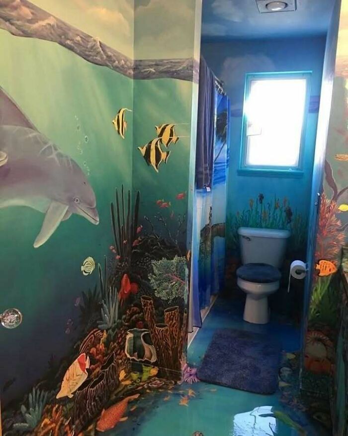 Bathroom with chaotic underwater mural featuring fish, coral, and a dolphin, blending trash and culture in a colorful design.