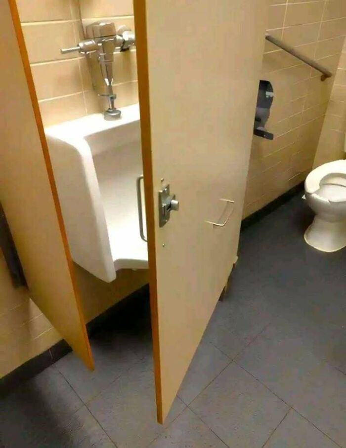 Public bathroom stall with a door that blocks the urinal, highlighting hilariously dumb engineering mistakes.