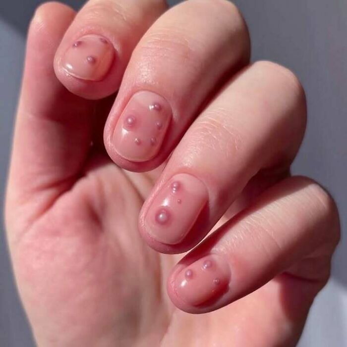 Close-up of a hand with transparent nails featuring raised bubble-like details, blending chaotic culture and visual trash.