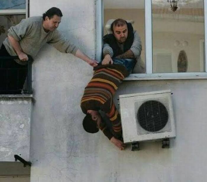 Two men attempting a risky air conditioner repair, illustrating hilariously dumb engineering mistakes in progress.