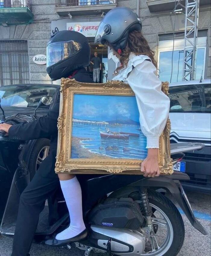 Two people on a scooter wearing helmets, with one holding a framed artwork, blending culture and chaotic trash humor.