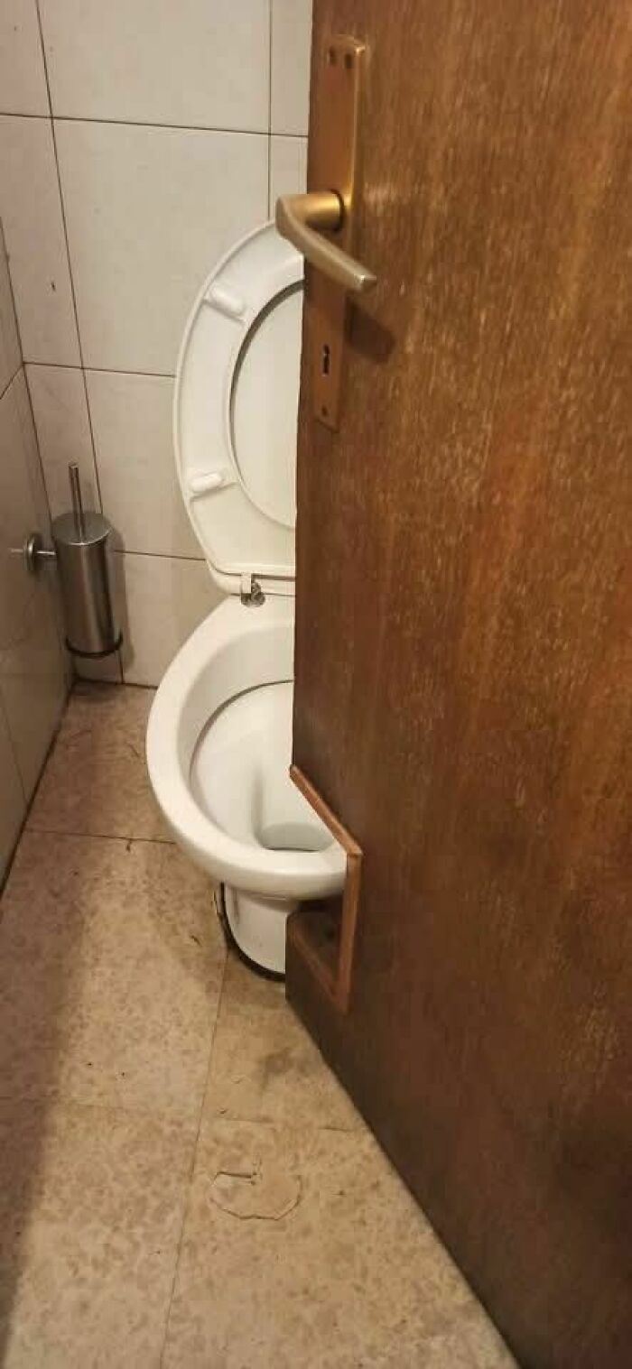 Bathroom door with a toilet cutout design, illustrating hilariously dumb engineering mistakes in a small space.