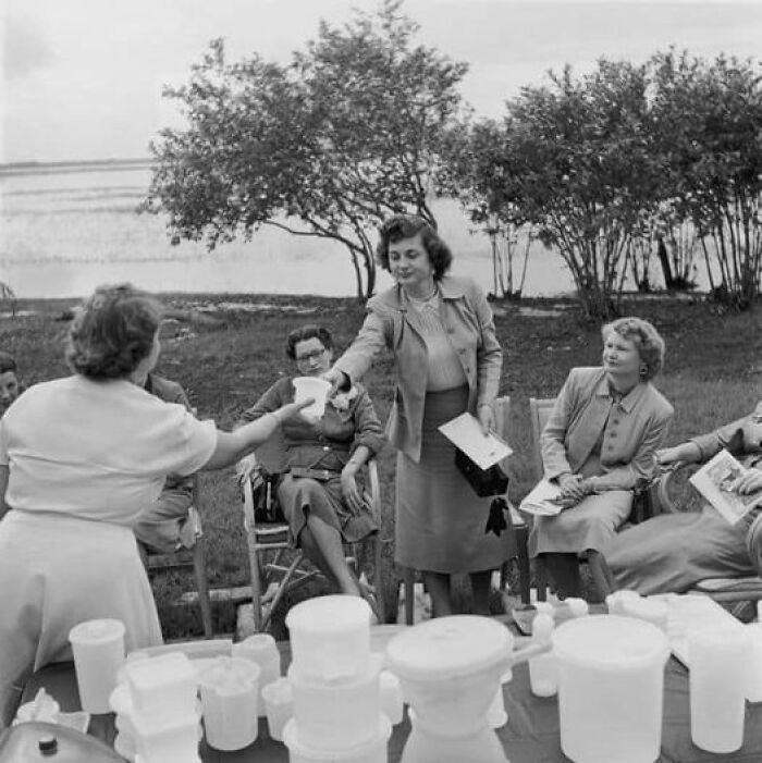 Women exchanging documents outdoors surrounded by vintage containers in a unique old photo capturing a historic moment.