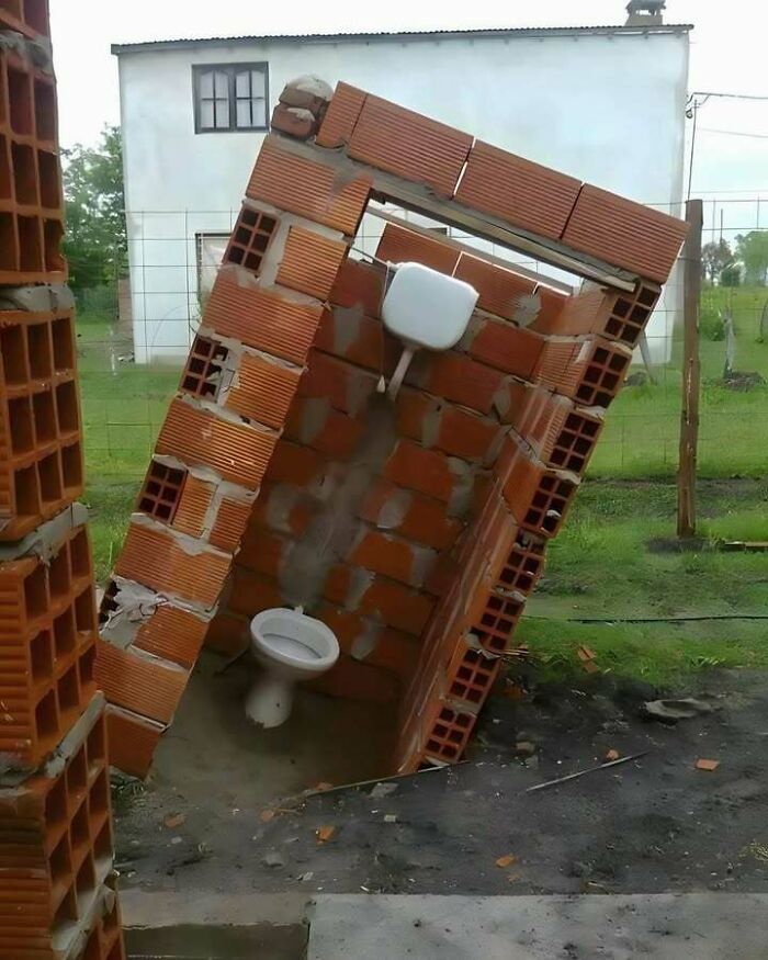Toilet stall made of bricks leaning and collapsing outdoors showing engineering fails and dumb mistakes.
