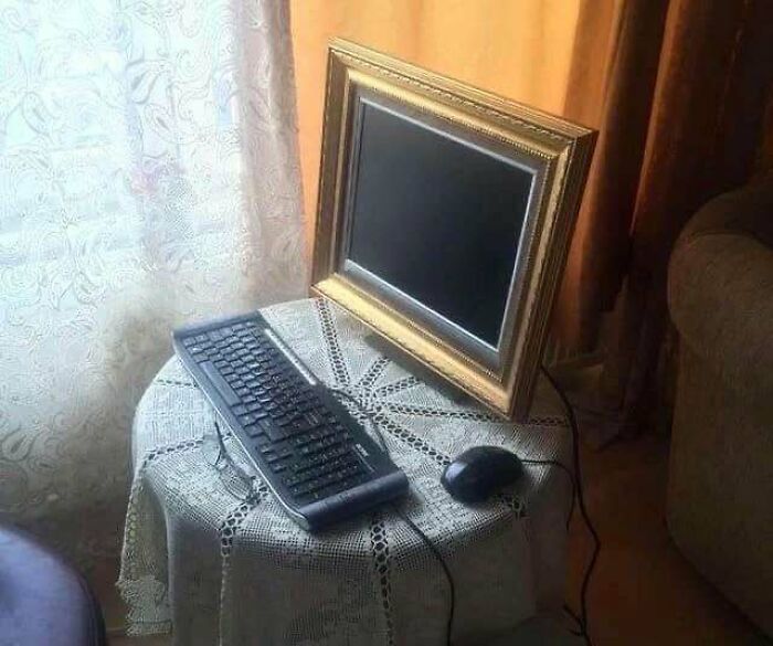 Keyboard and mouse placed on a small table with a picture frame used as a computer monitor in a chaotic cultural setting.