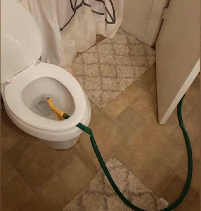 Toilet with a garden hose awkwardly running through a door and inserted inside the bowl, a hilarious engineering mistake.