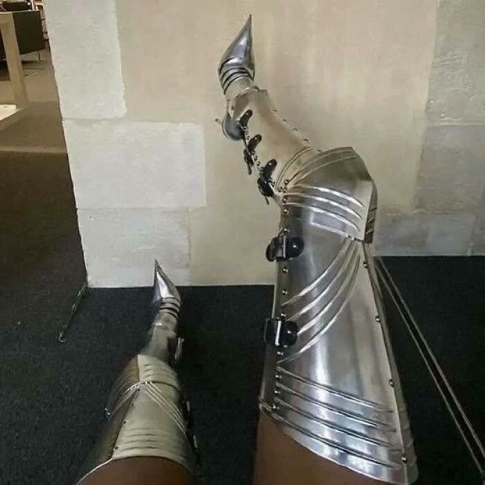 Legs wearing shiny silver armor boots resting indoors, combining chaotic culture and trash vibes in a humorous way.
