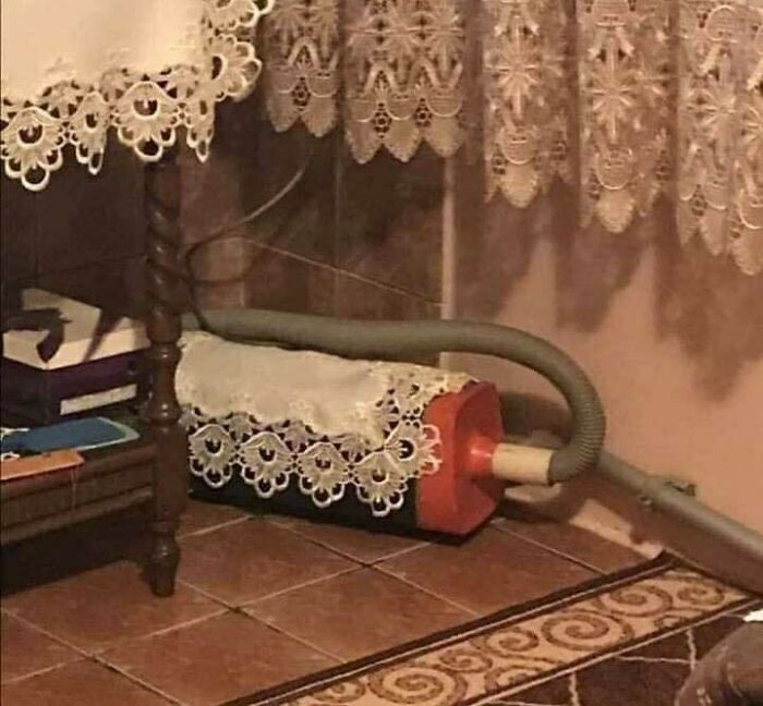 Vacuum cleaner covered with lace doilies blending trash and culture in a chaotic, humorous home setting.