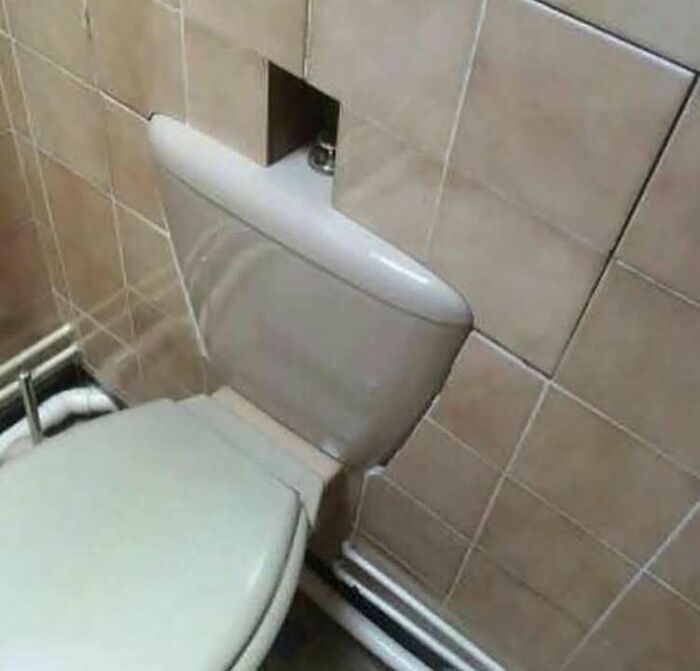 Toilet cistern installation showing a hilariously dumb engineering mistake with tiles cut incorrectly around it in a bathroom.