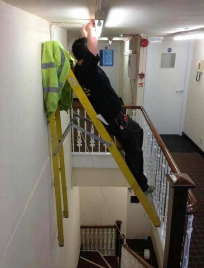 Man dangerously leaning backward on a ladder over a stairwell, showcasing hilariously dumb mistakes despite engineering degrees.