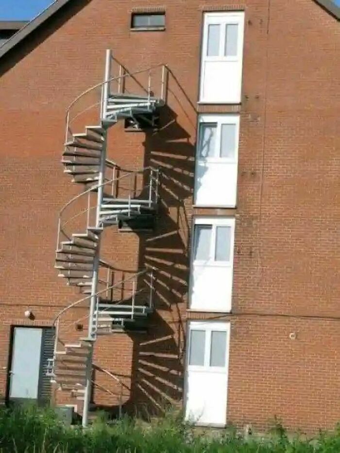 Spiral staircase with no access points on a brick building wall illustrating engineering mistakes humorously.