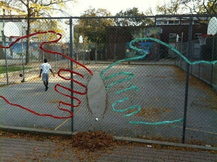 Chain-link fence with colorful graffiti hands reaching towards each other at an outdoor basketball court, blending trash and culture.