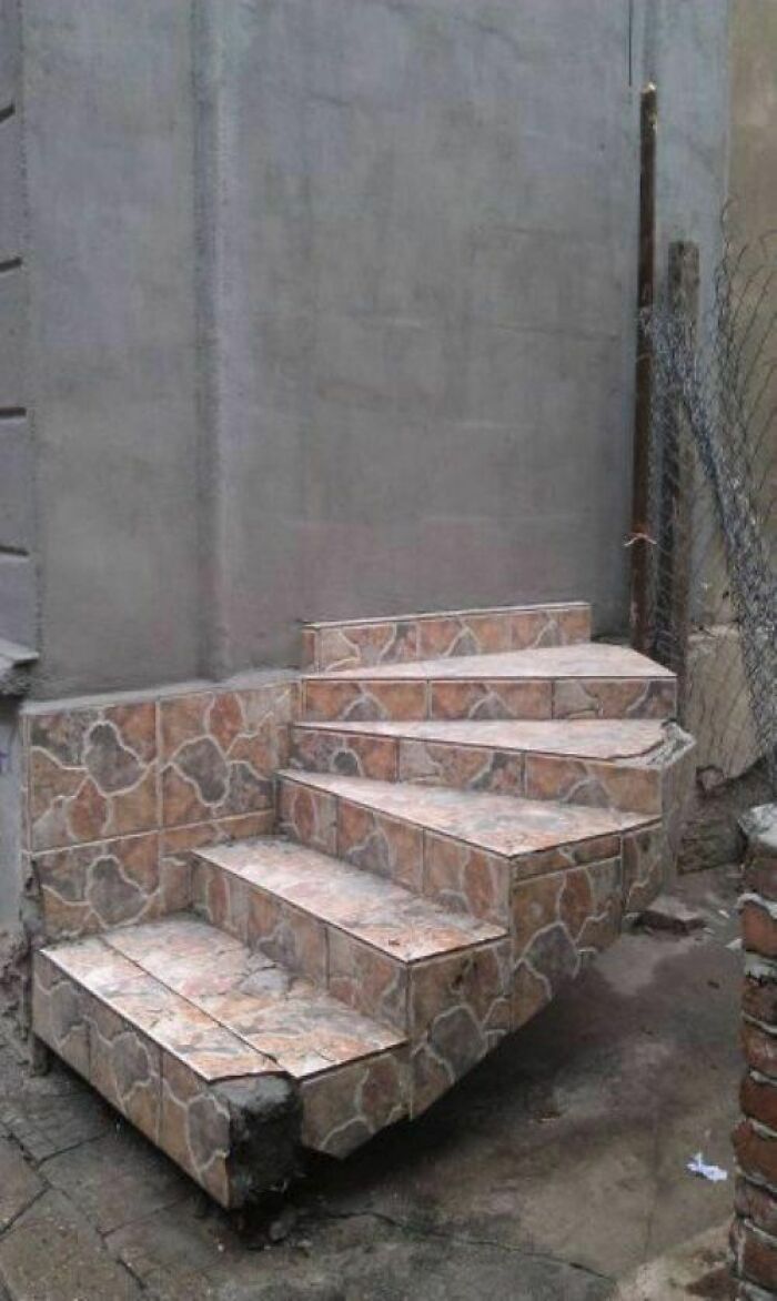 Concrete stairs with broken bottom step and poor engineering mistakes in construction causing safety hazards outside a building