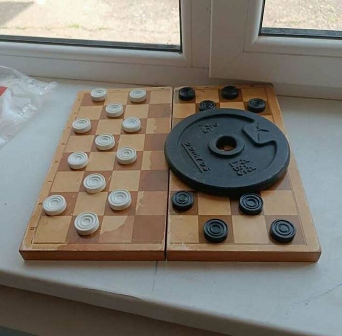 Checkerboard game disrupted with a weight plate on part of the board, combining trash and culture in a chaotic way.