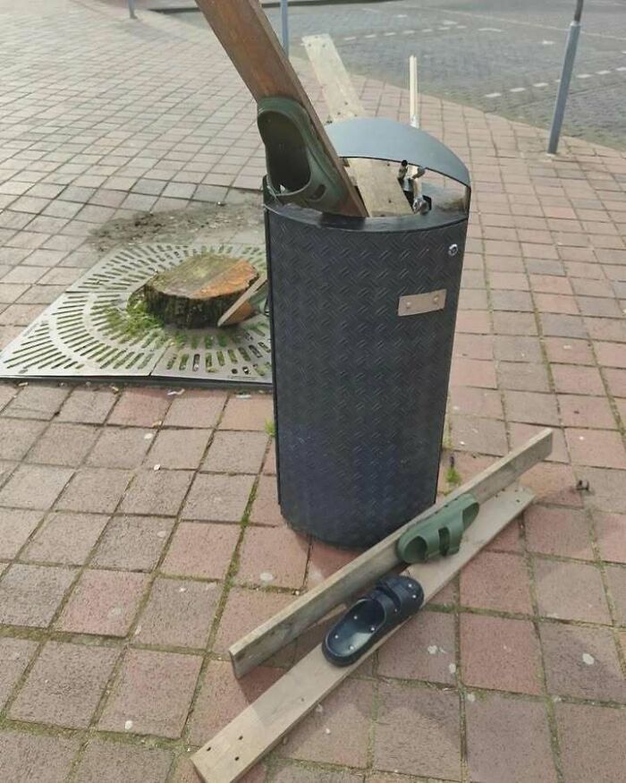 Outdoor trash bin filled with wooden planks and sandals, showcasing chaotic mix of trash and culture on sidewalk.