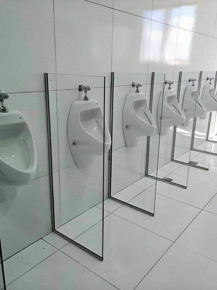 Men’s restroom urinals with transparent glass dividers, showcasing hilariously dumb engineering mistakes in design.