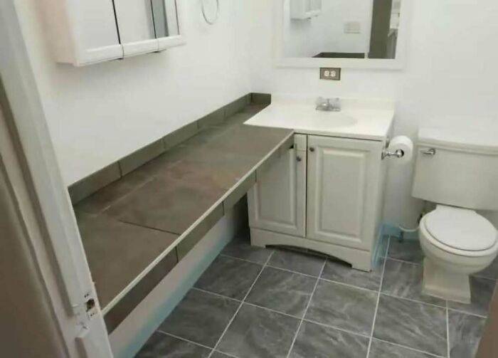 Bathroom with an unusual engineering design showing a long counter obstructing space above the toilet area.