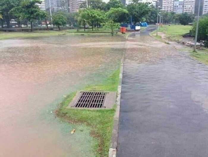 Flooded park pathway contrasted with a raised drainage grate highlighting hilariously dumb engineering mistakes.