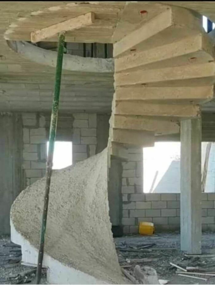 Incomplete concrete spiral staircase under construction with a temporary support pole, showing engineering mistakes.