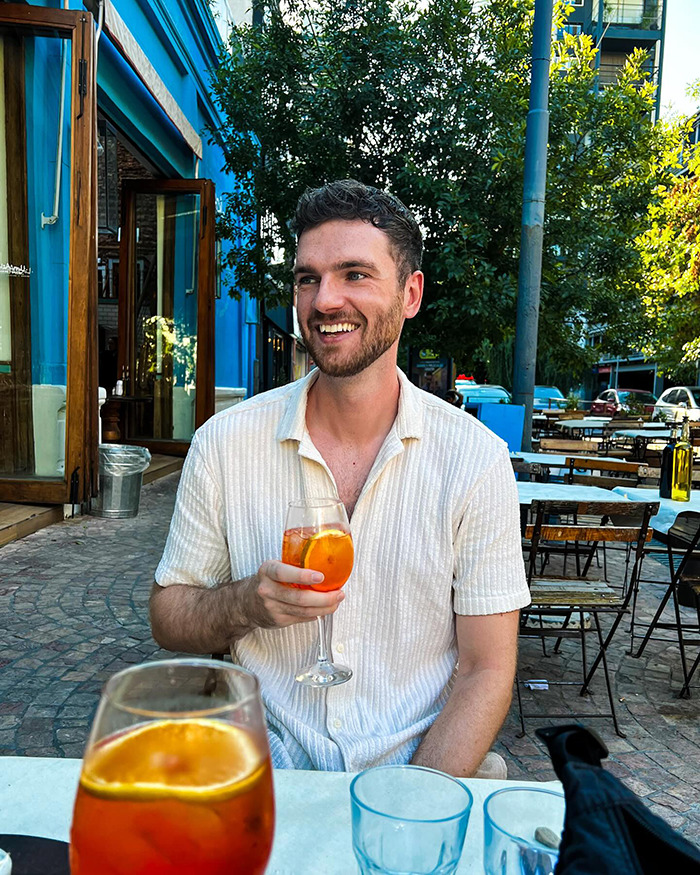 Man smiling and holding a drink outdoors at a cafe, related to passenger allergy request announcement on a flight debate. Man smiling and holding a drink outdoors at a cafe, related to passenger allergy request announcement on a flight debate.