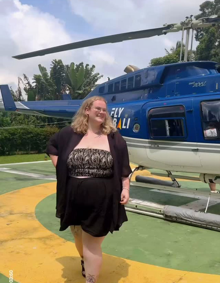 Plus-size traveler smiling outdoors near a blue helicopter, illustrating plus-size traveler experiences in aviation travel.