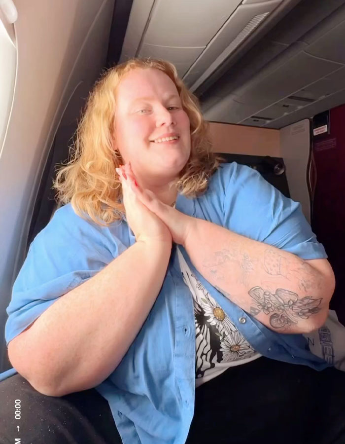 Plus-size traveler smiling on airplane, sharing reasons for not booking two airline seats, facing criticism.
